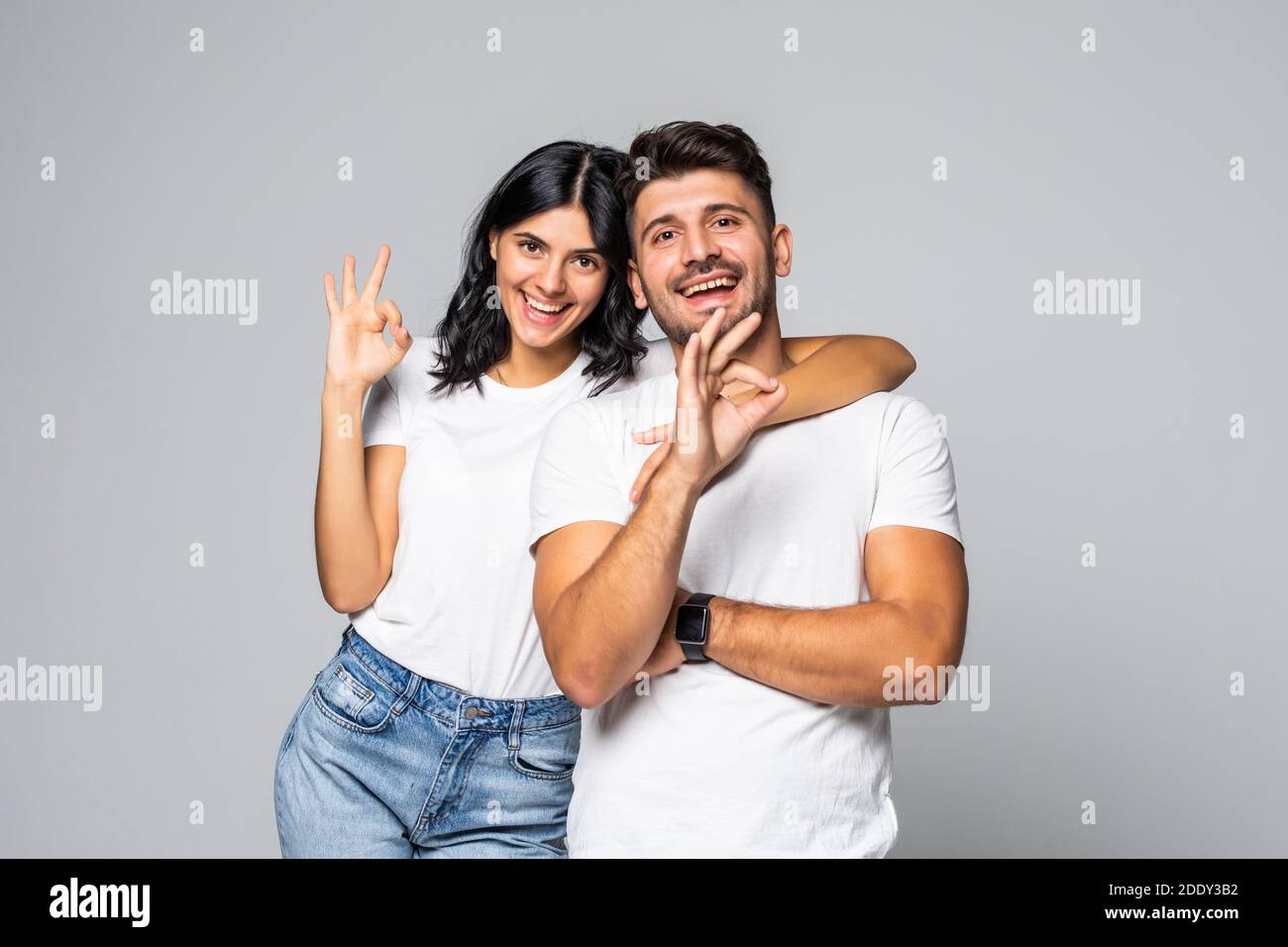 Full length portrait of a cheerful smiling couple hugging and showing ...