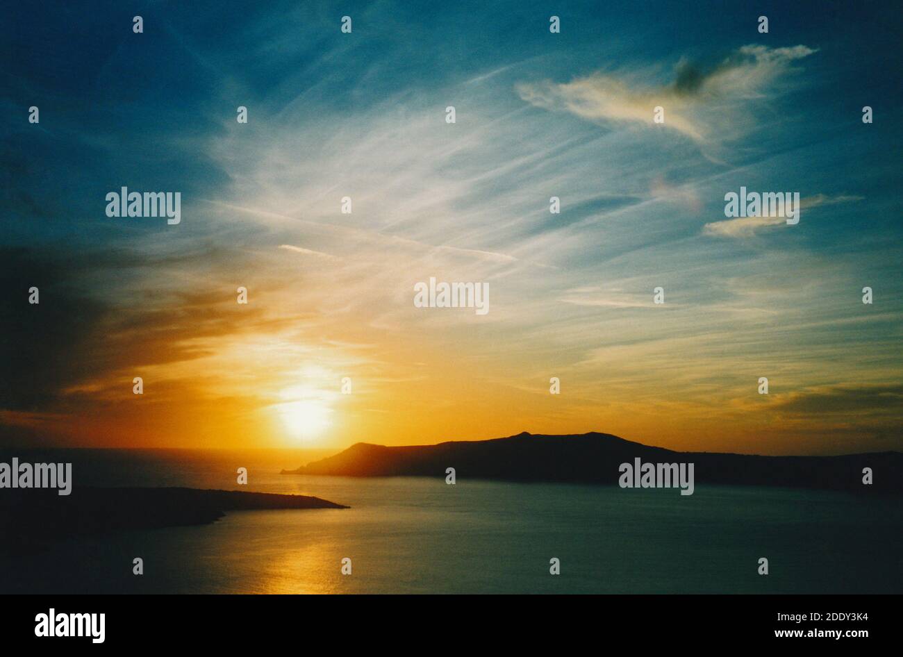 View from Thira (Thera) town of the sun setting over the caldera and Aegean Sea, with Thirasia and Nea Kameni islands silhouetted; Santorini, Greece Stock Photo