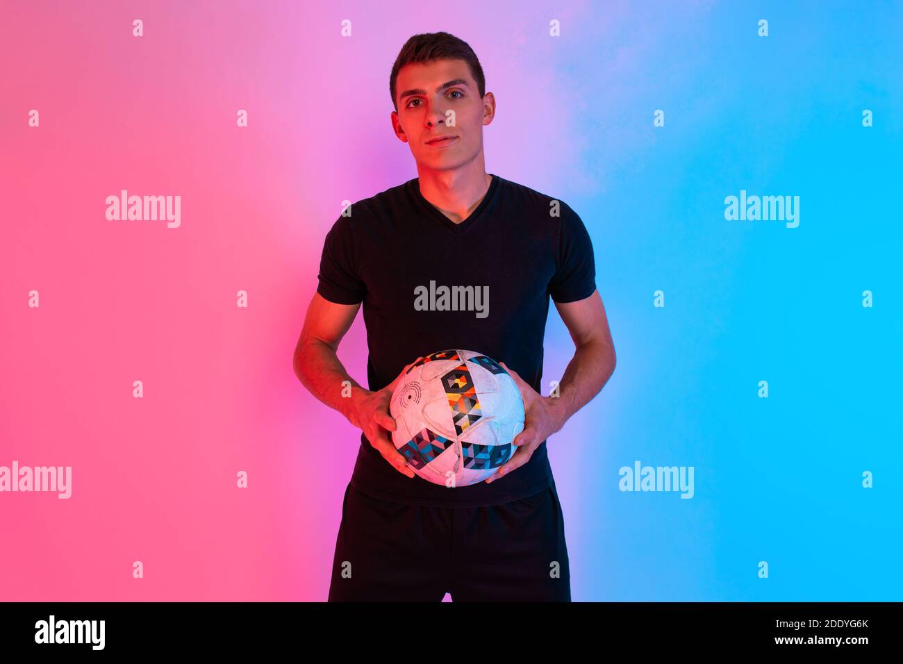 Football player in sportswear, posing holding a football, standing on a background with red and blue neon light Stock Photo