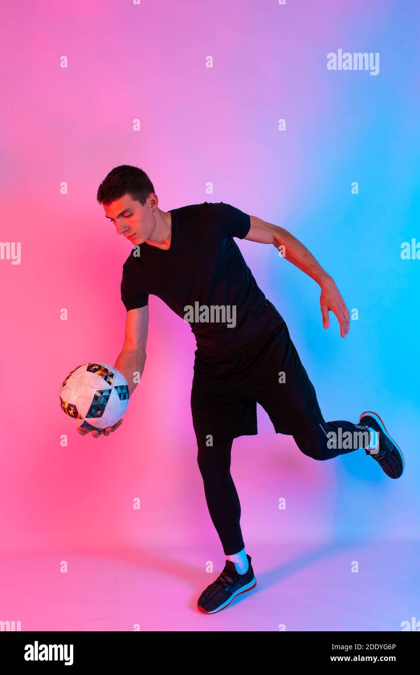 Football player in sportswear, a man playing with his feet with a ball on an isolated red and blue neon background Stock Photo