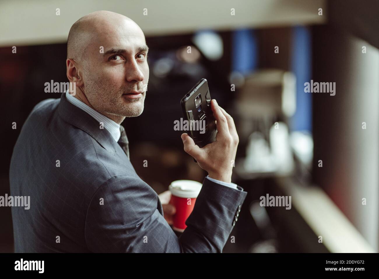 Bald businessman looking at camera turned from back. Caucasian man wearing a business suit, glasses and tie talking on cell phone while getting down Stock Photo