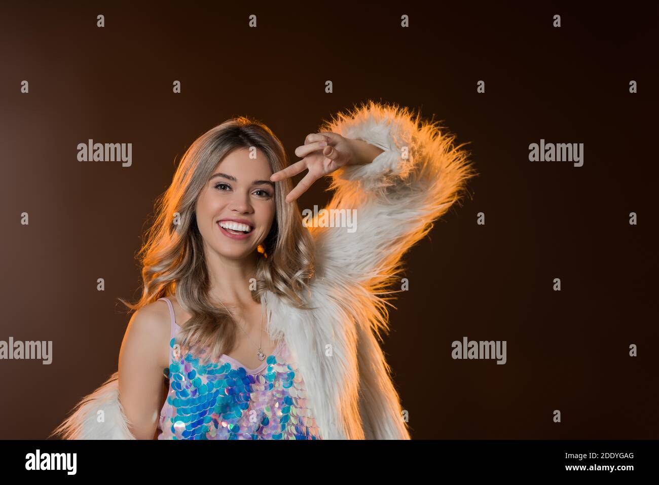 pleased blonde woman in faux fur jacket showing peace sign on black ...