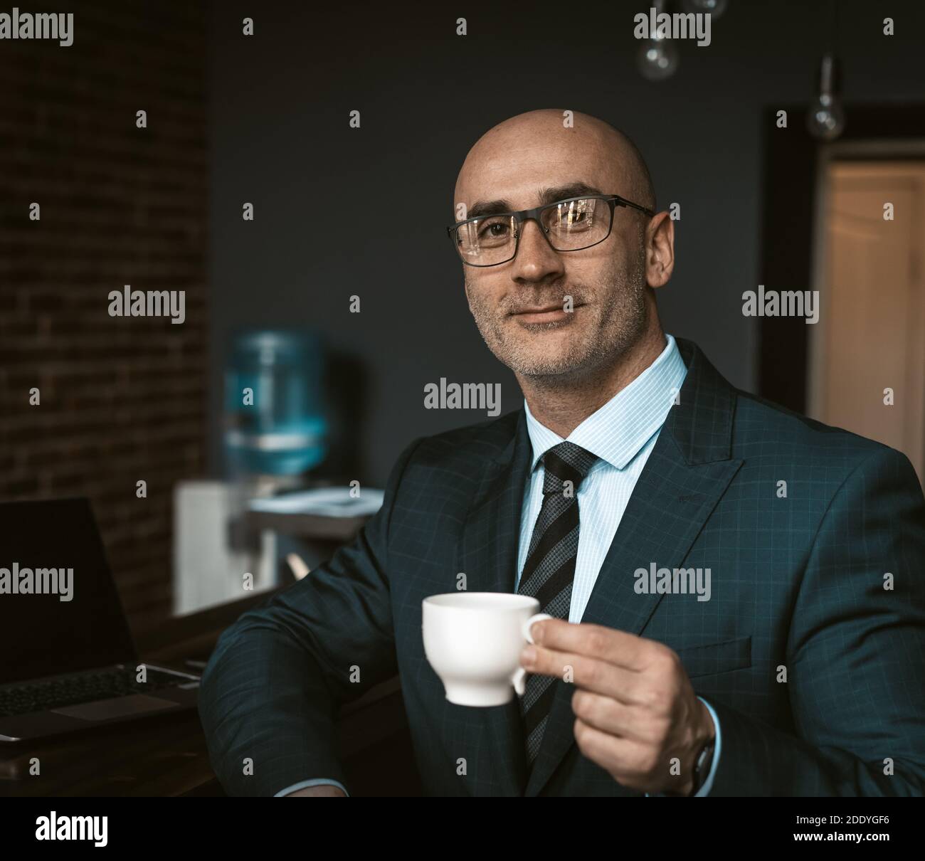 Mature business man in a business suit, holding a cup of coffee in a office building cafeteria having and looking at camera wearing expensive suit and Stock Photo