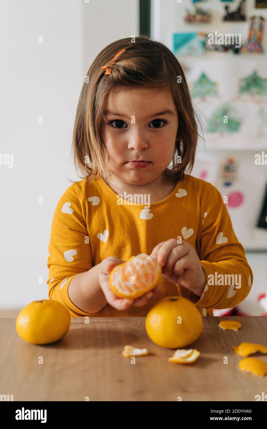 Caucasian girl peeling tangerines on kitchen counter. Healthy child