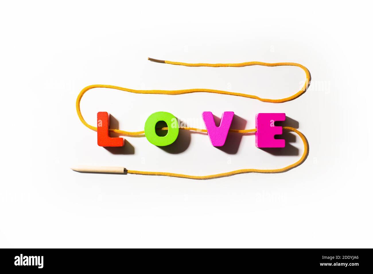 Wooden colorful letters with word Love from colorful letters with holes, strung on a lace in snake shape, with shadows at white background, main word, Stock Photo