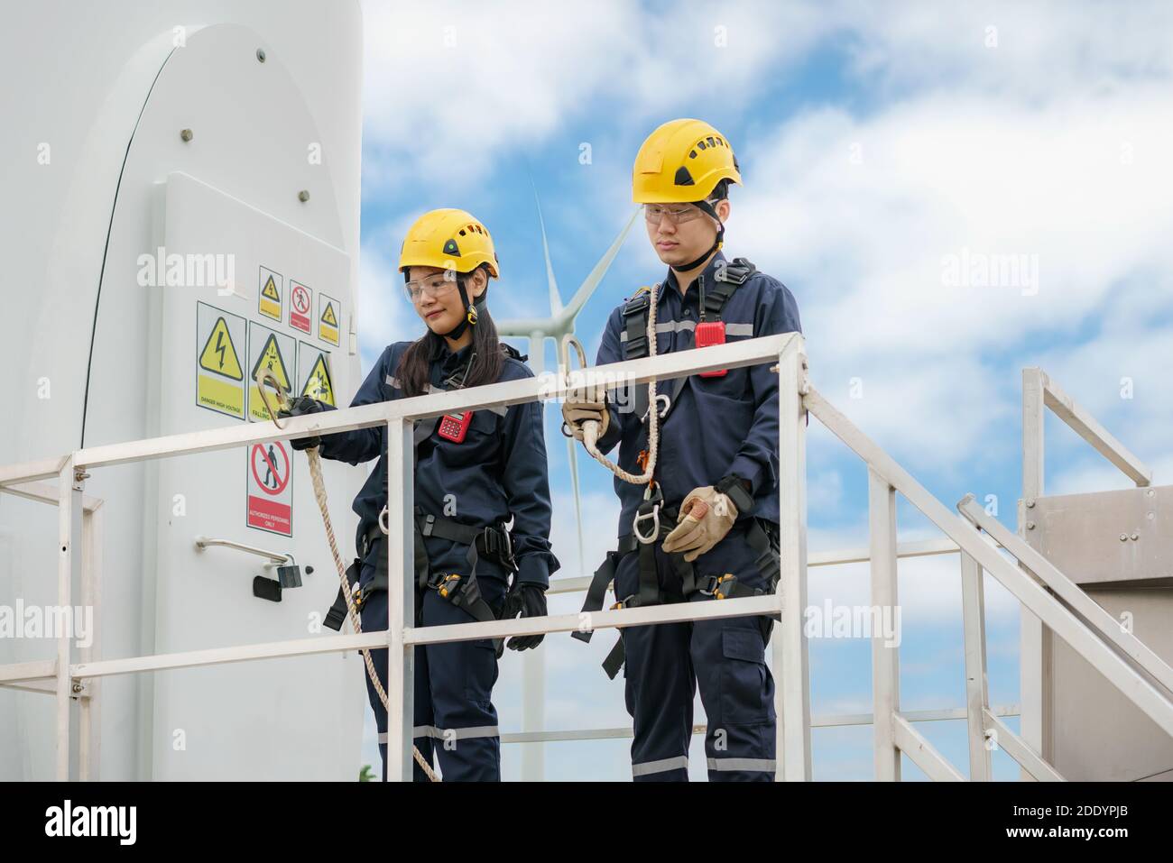 Asian man and woman Inspection engineers preparing and progress check of a wind turbine with safety in wind farm in Thailand. Stock Photo