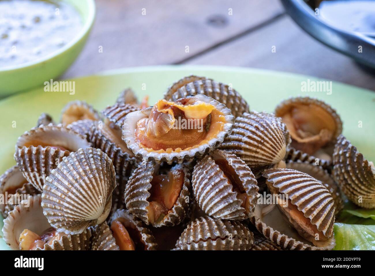 Steamed cockle or Boiled cockles on the dish with spicy seafood sauce and vegetable in restaurante wooden background Stock Photo