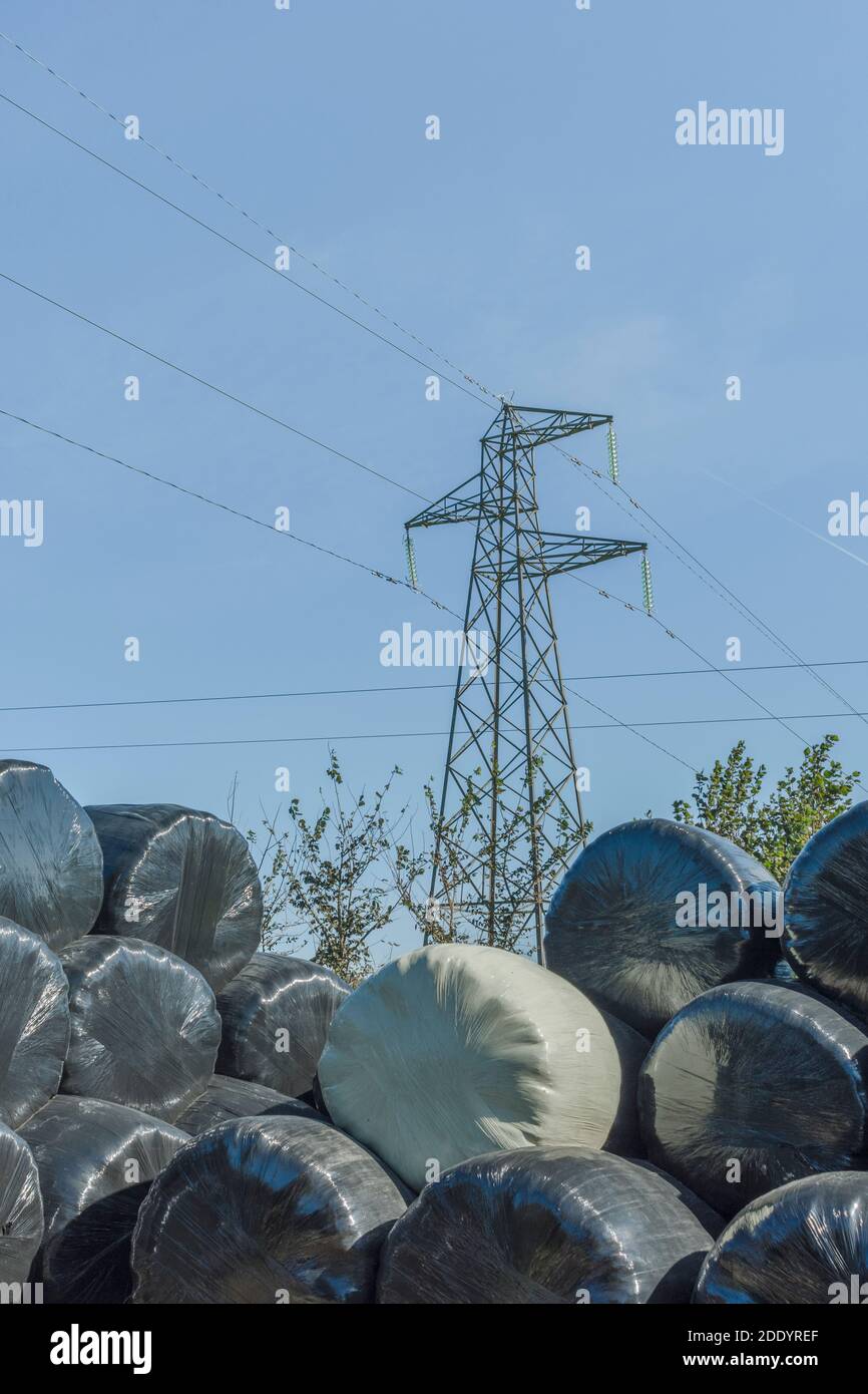 High voltage electricity pylon & polywrap hay bales against blue summer
