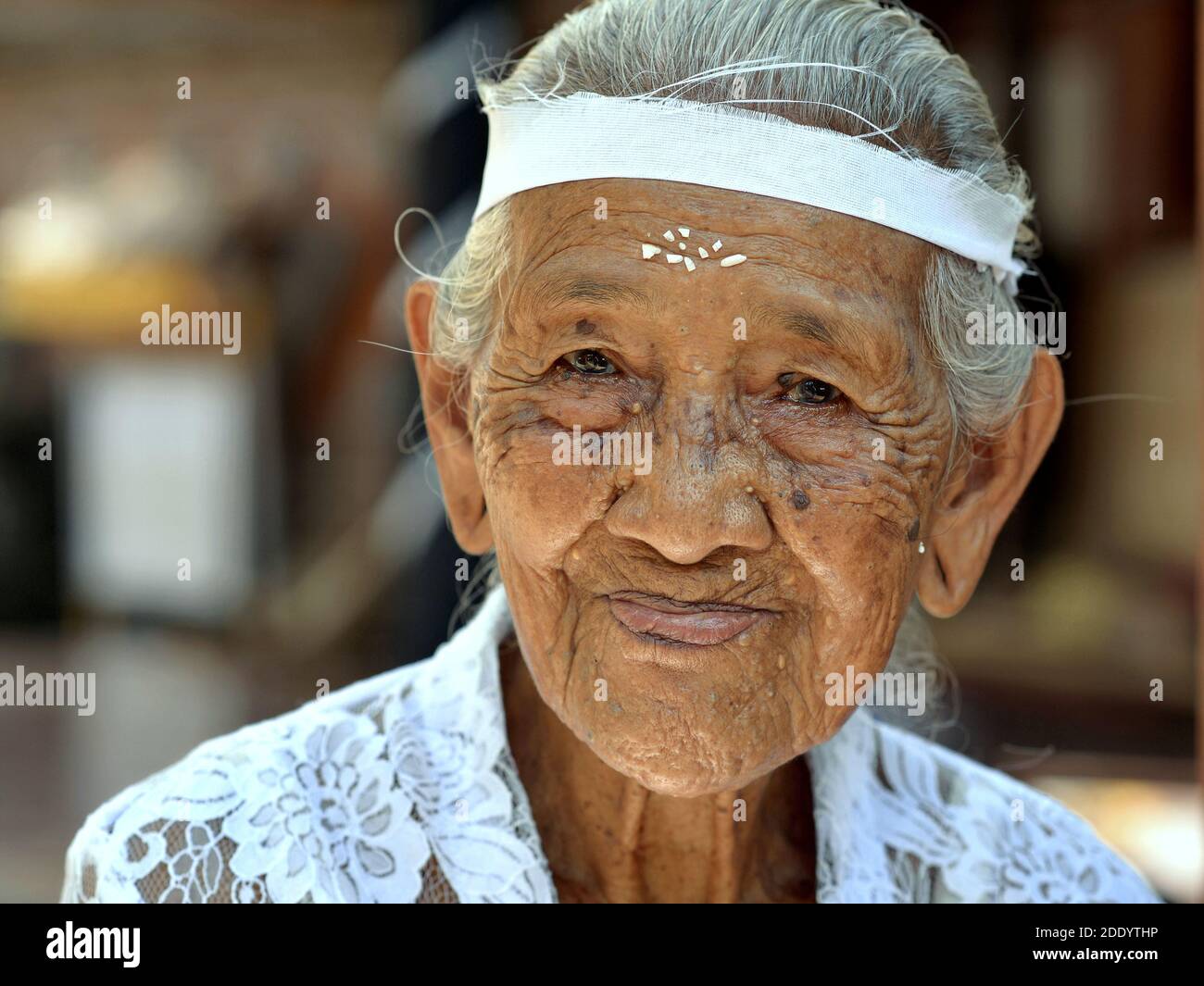 Old Indonesian Balinese woman with rice grains on her forehead wears a white traditional kebaya blouse during a religious Hindu ceremony. Stock Photo