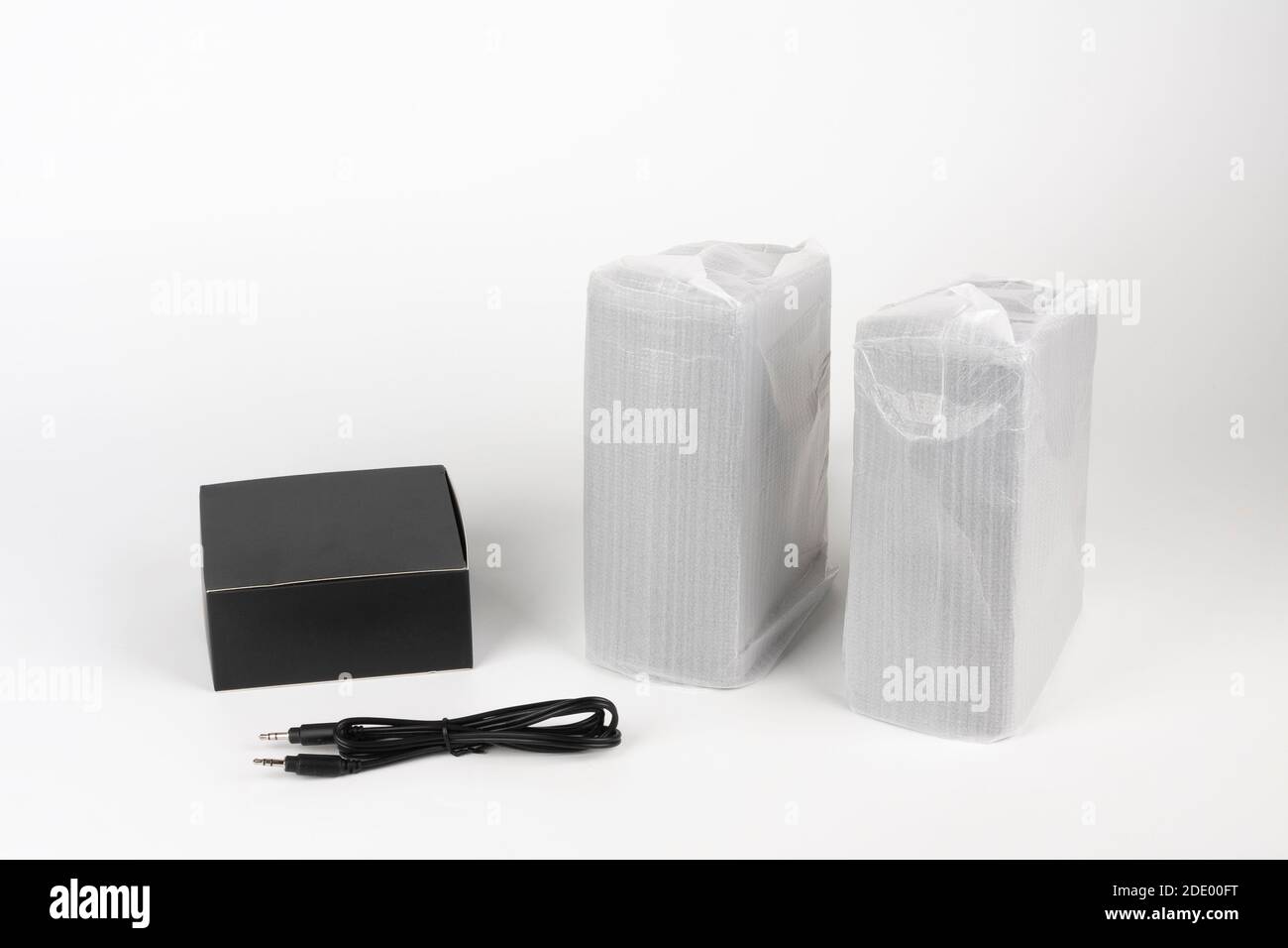 Two computer speakers in plastic bag on white background. Black box