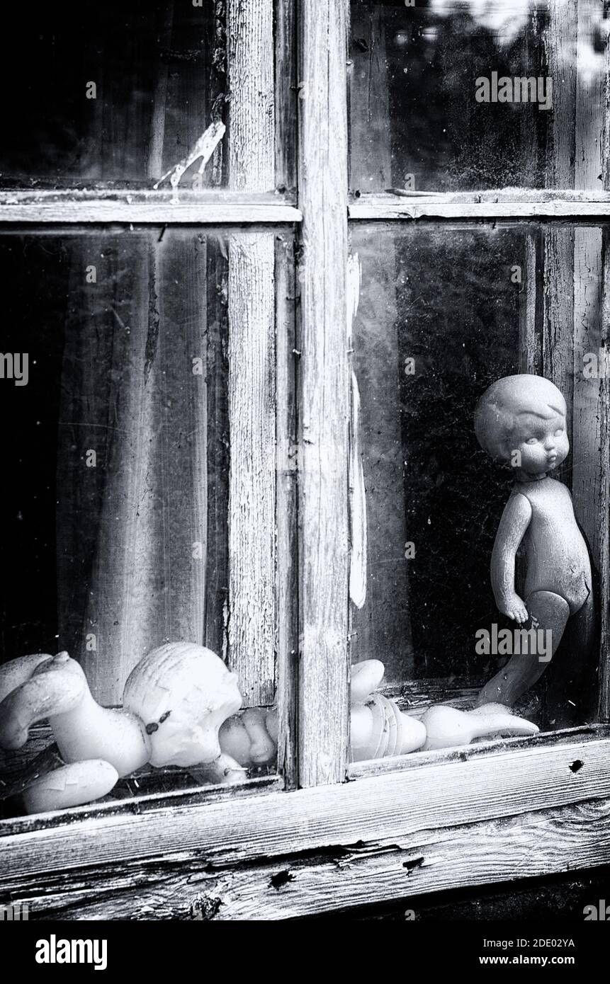 Black and white concept window frame with Soviet dolls without a trademark in an abandoned house vertical orientation (Pskov region, Russia) Stock Photo