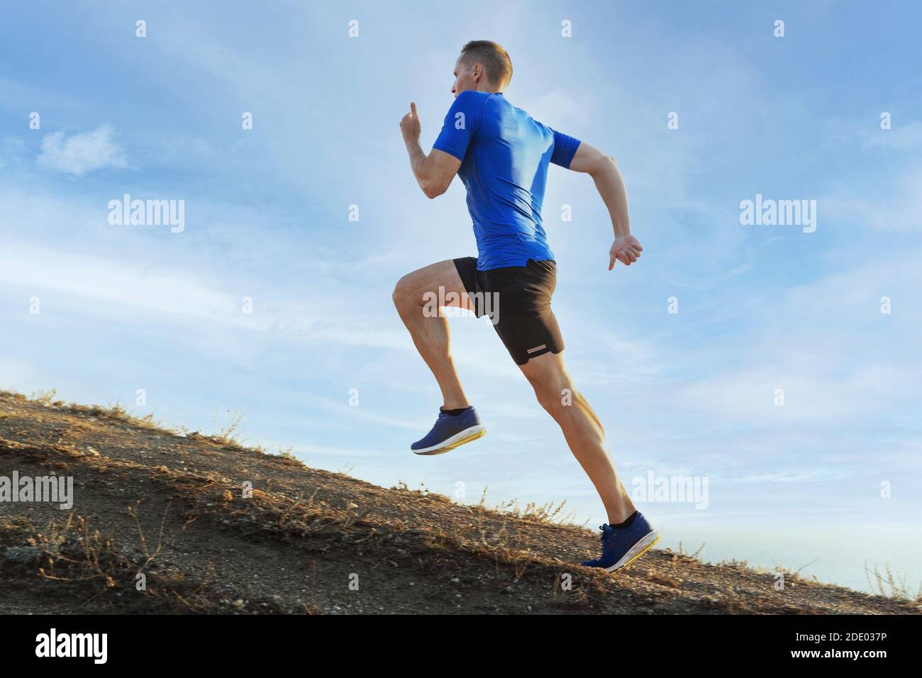 man athlete runner running uphill in background blue sky Stock Photo ...