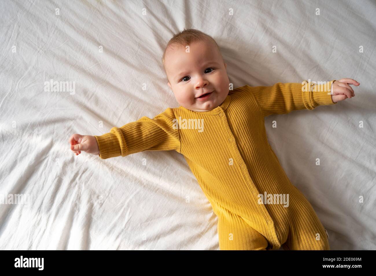 Laughing happy little infant baby boy with open mouth moving hands and legs view from above Stock Photo