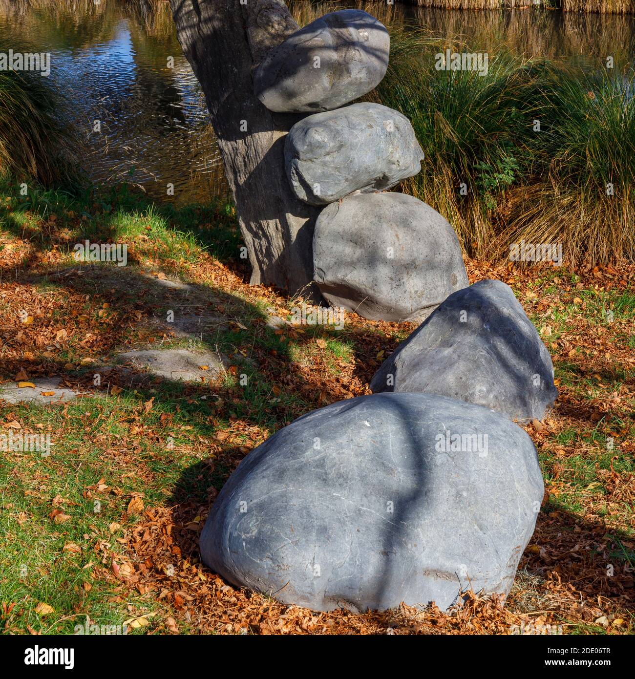 Public art beside the Avon River in central Christchurch, New Zealand. Boulders arranged in a snake like order exiting from a tree. Stock Photo