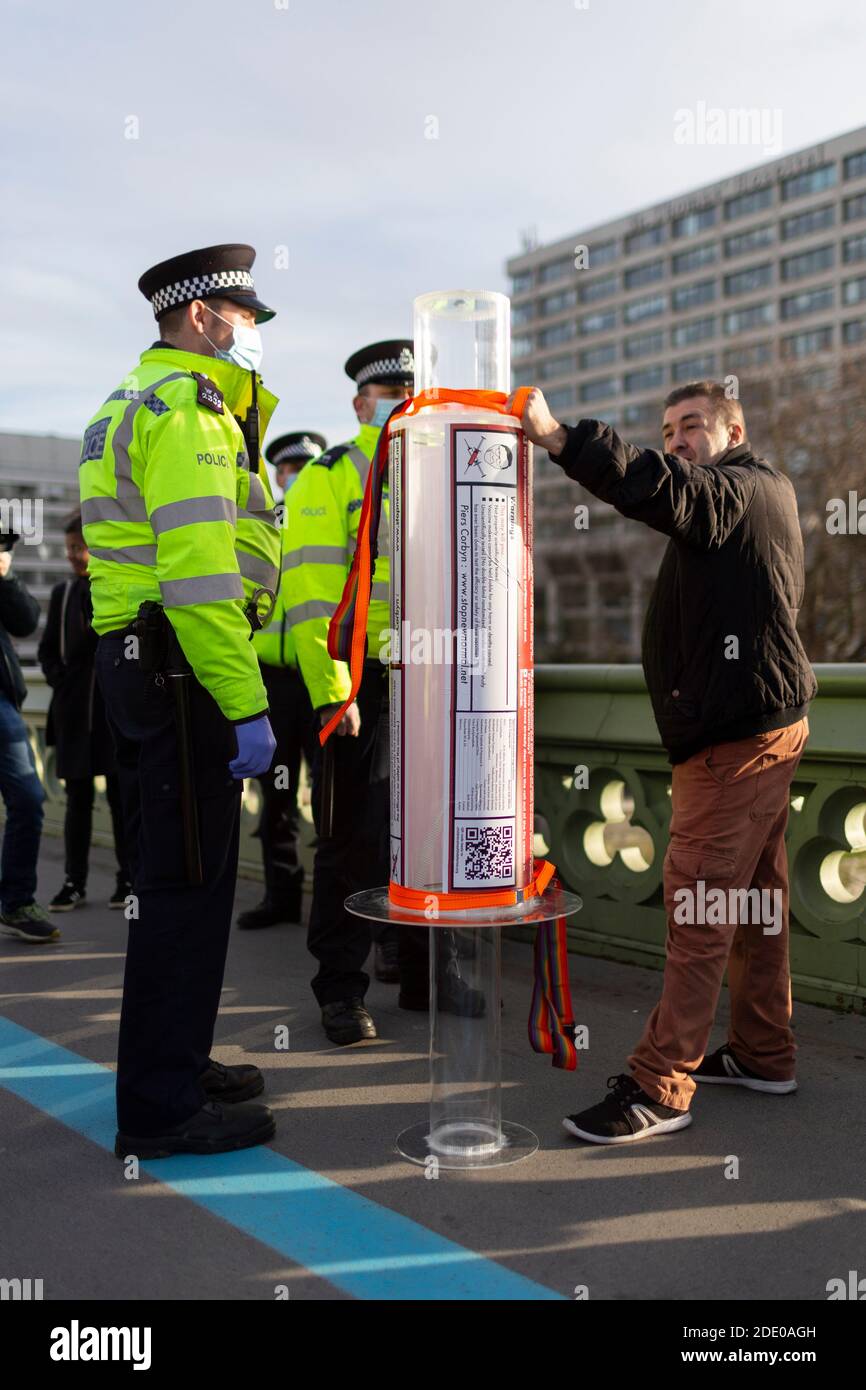 Police detain protester with giant syringe during anti-vaccination protest, Westminster Bridge, London, 24 November 2020 Stock Photo