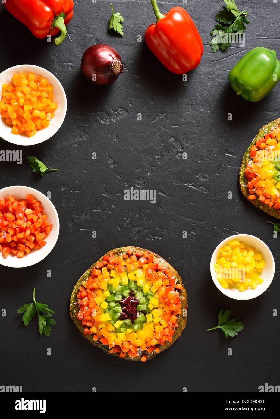 Frame of rainbow veggie bell peppers pizza and ingredients on black stone background with free text space. Vegetarian vegan or healthy food concept. G Stock Photo