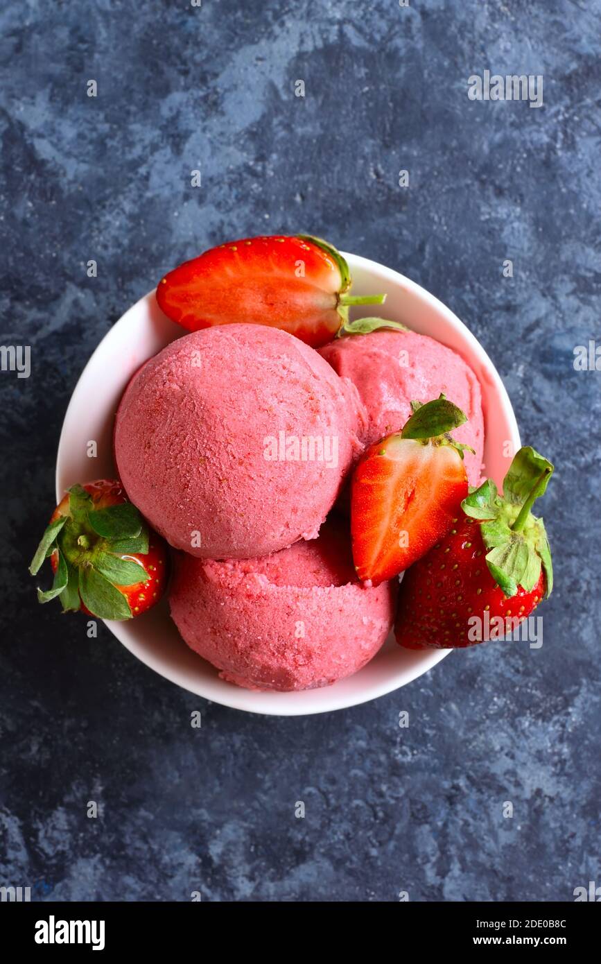 Strawberry ice cream scoop with fresh strawberries in bowl over blue stone background. Tasty summer cold dessert. Close up view Stock Photo