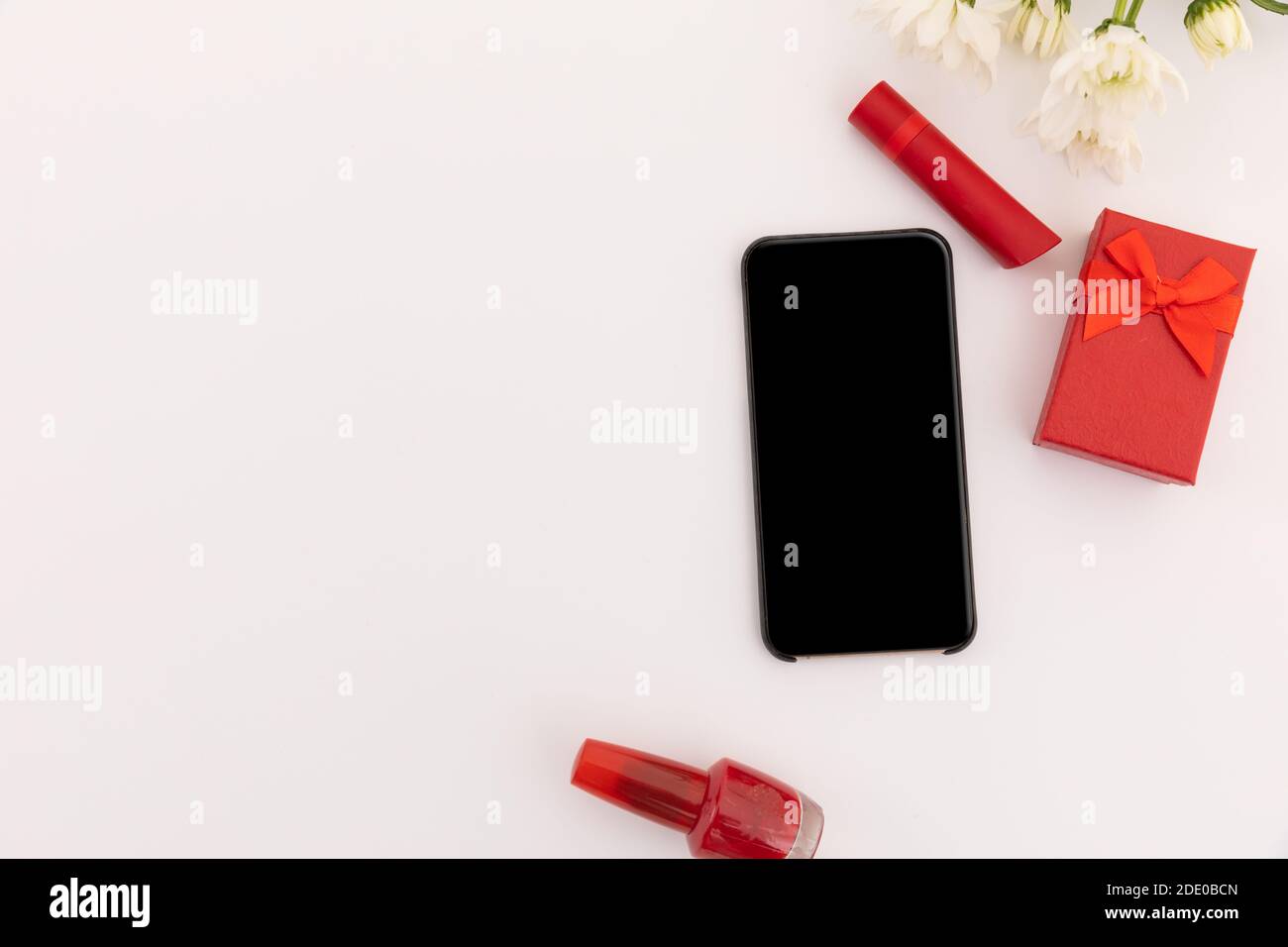 Smartphone, red lipstick, nail varnish, present and flowers on white background Stock Photo