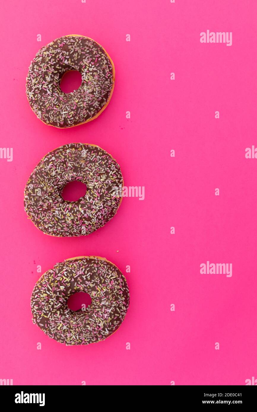 High angle view of three chocolate donuts with sprinkles on pink background Stock Photo