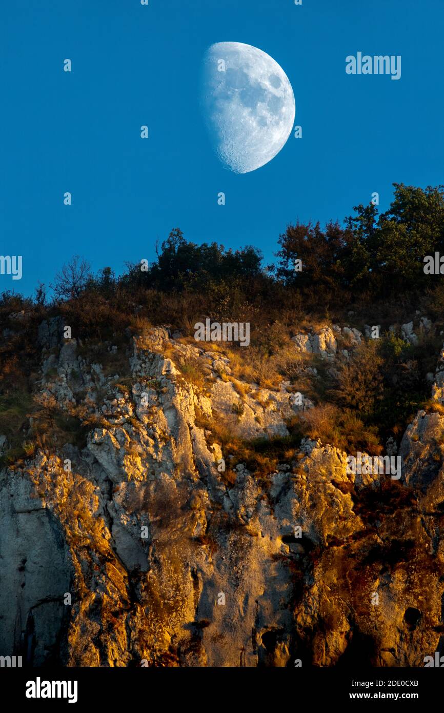 Cliffs above the Ardeche river are streaked with the light of the setting sun as the moon rises above them. Stock Photo