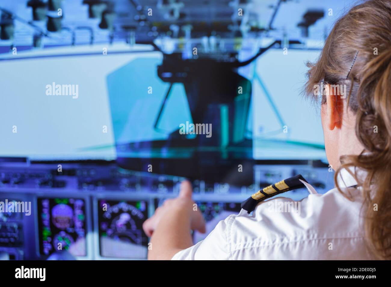 Beautiful woman pilot wearing uniform with epauletes changes the autopilot settings in the cockpit of a flying airplane Stock Photo