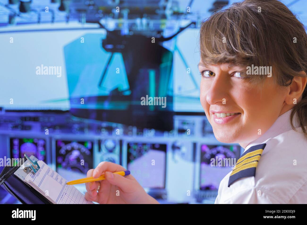 Beautiful woman pilot wearing uniform with epauletes, writting on notepad inside airliner Stock Photo
