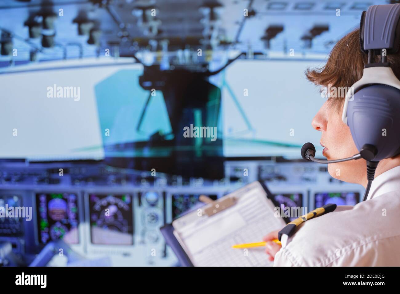 Beautiful woman pilot wearing uniform with epauletes and headset, writting on notepad inside airliner Stock Photo