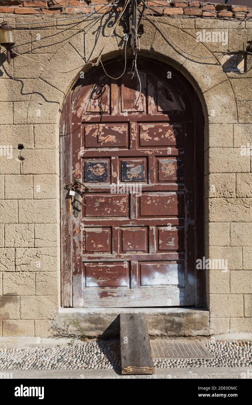 Old distressed brown painted arched wooden doors on facade of abandoned cut stone house, Old Town of Rhodes, Rhodes, Greece Stock Photo