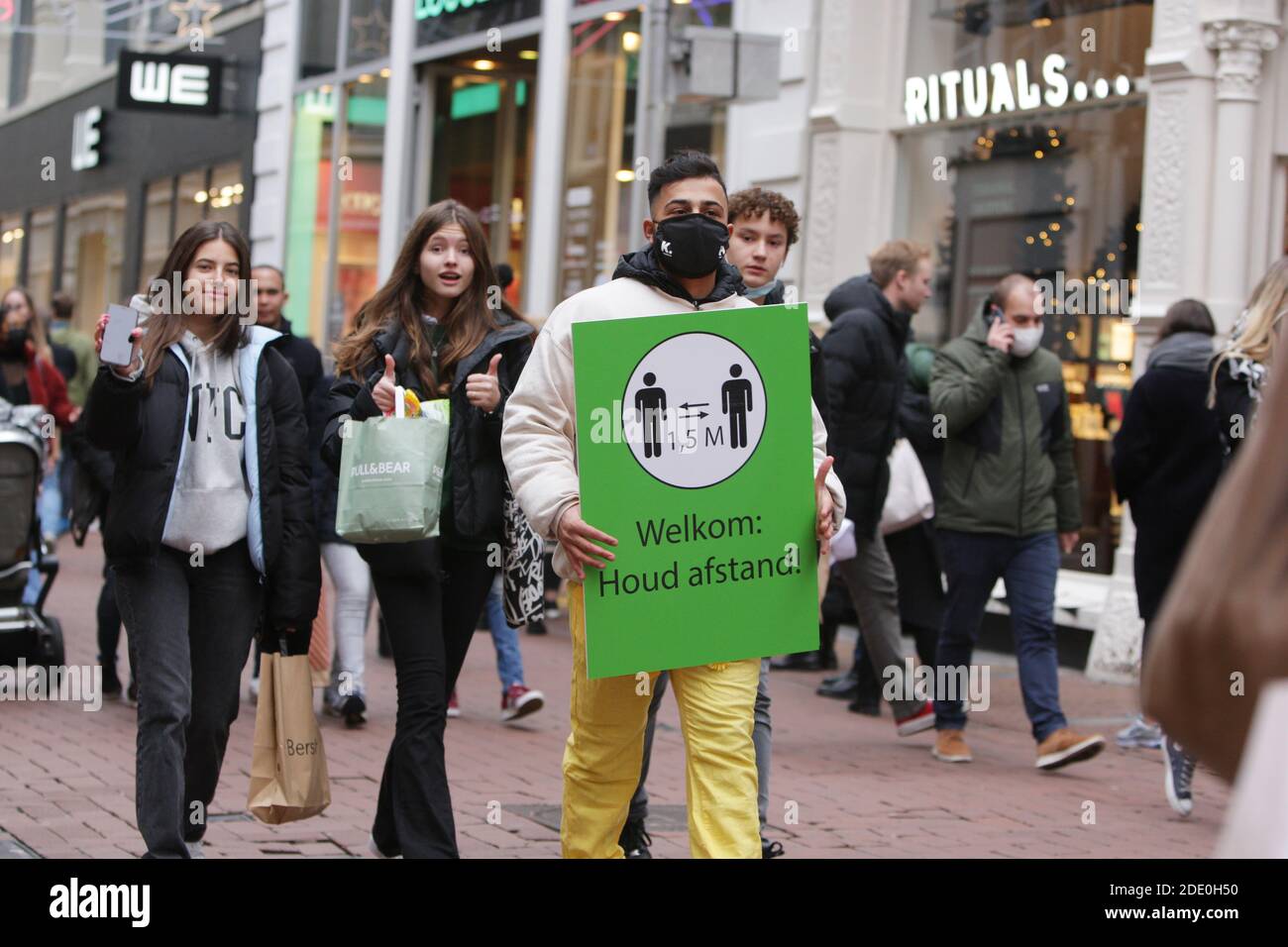 A municipal employee hold a placa for consumers to avoid busy places and keep social distance during 'Black Friday' at the shopping street Kalverstraa Stock Photo