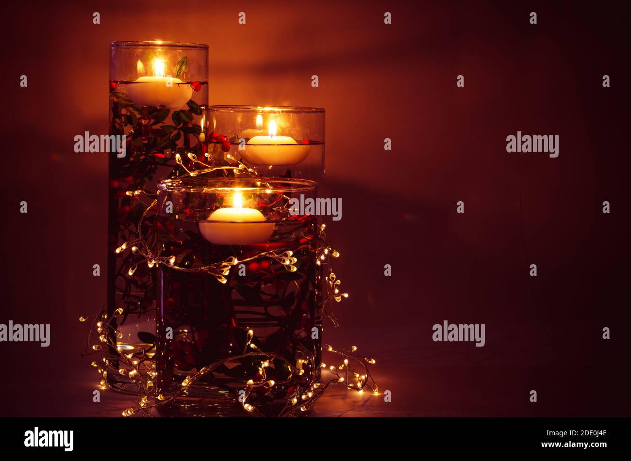 burning candles floating on water in vase full of water and colorful flowers in dark background