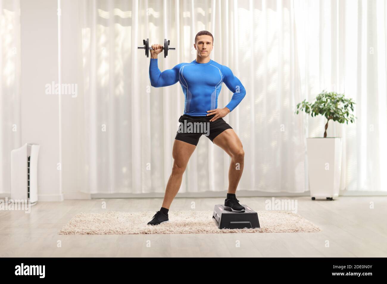 Bodybuilder exercising aerobic on a stepper and holding weights at home Stock Photo