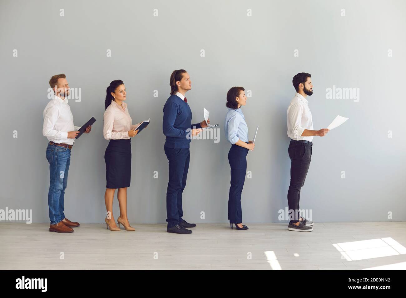 Young candidates for vacancy or job seekers standing in line with resumes and waiting for interview Stock Photo