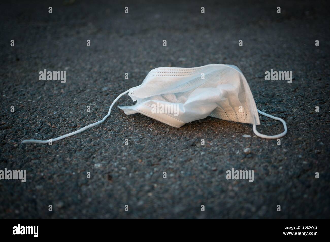 Crumpled used disposable protective medical mask on the asphalt. Black and white photo with vignetting Stock Photo