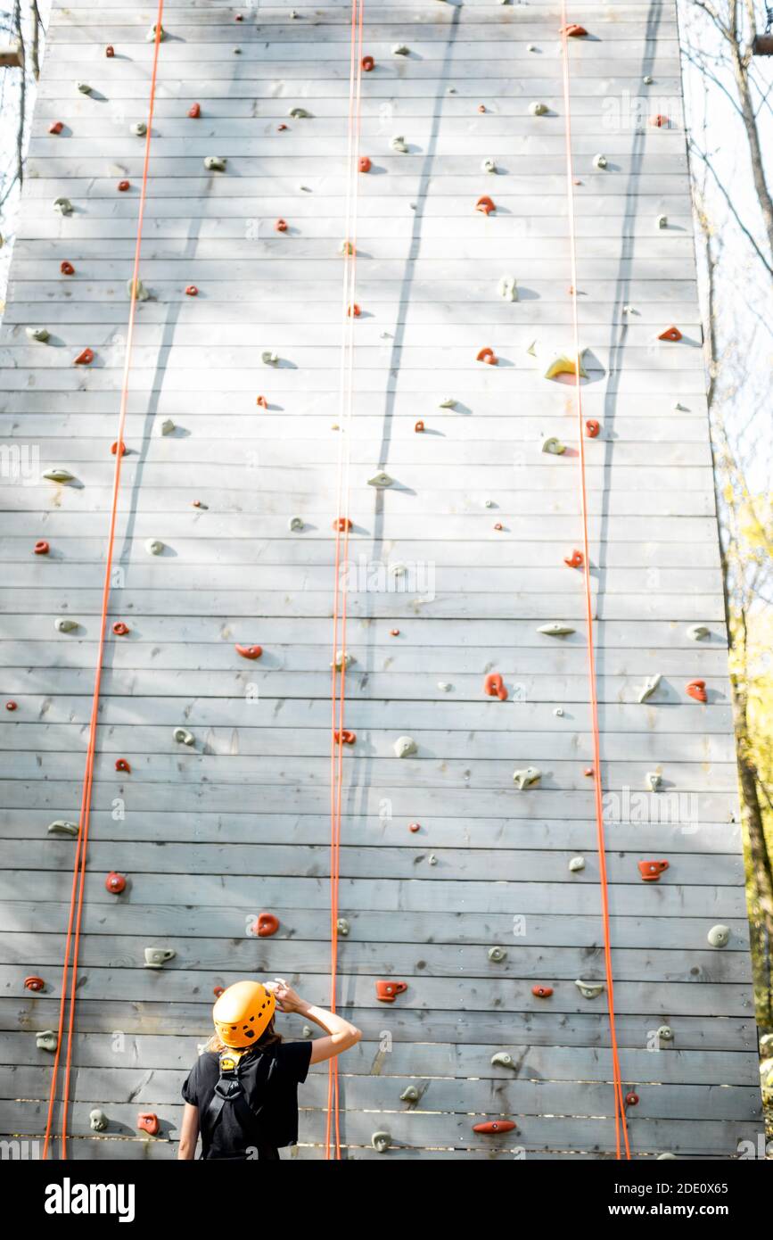 Young woman in sportswear and safety equipment looking on the climbing wall before climbing. Wide view from the backside Stock Photo