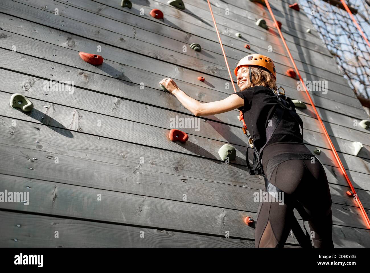 Young wellequipped woman climbing the wall outdoors in the park for