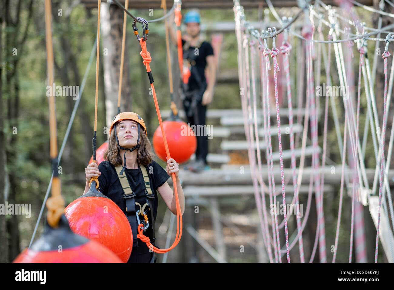 Well-equipped man and woman having an active recreation, climbing ropes in the park with obstacles outdoors Stock Photo