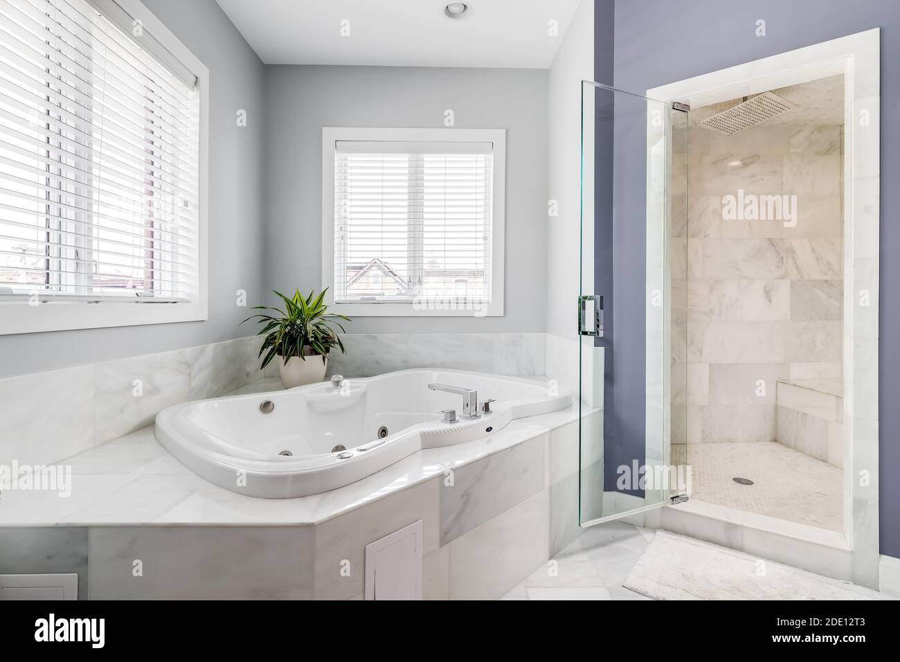 A large jacuzzi tub surrounded by marble tiles and a stand up tiled shower with a bench seat. Stock Photo
