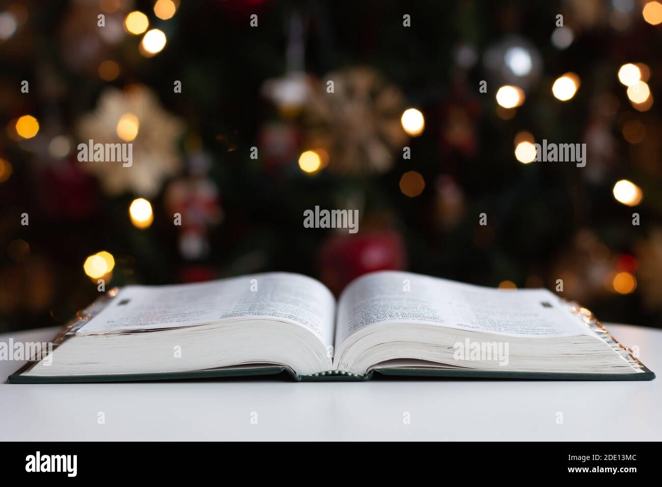 Bible on white table open in front of Christmas tree with lights, seasonal holiday background Stock Photo