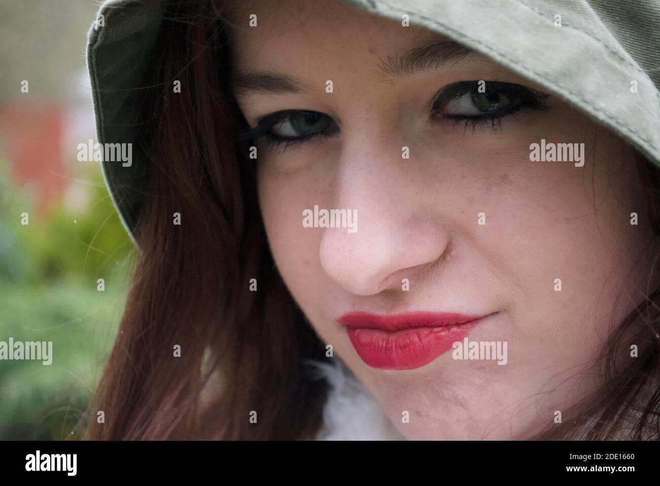 Pouting lips; the face of a lady wearing make up, with the hood of her raincoat pulled over her head to keep her dry from the weather Stock Photo