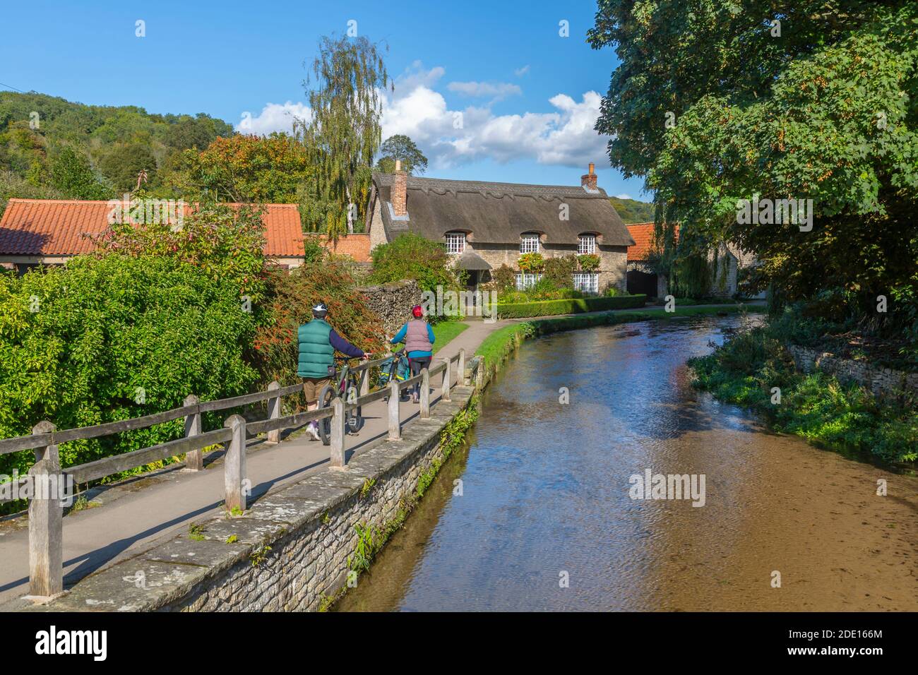 View of cyclists, riverside thatched cottage and Thornton Beck, Thornton Dale, North Yorkshire, England, United Kingdom, Europe Stock Photo