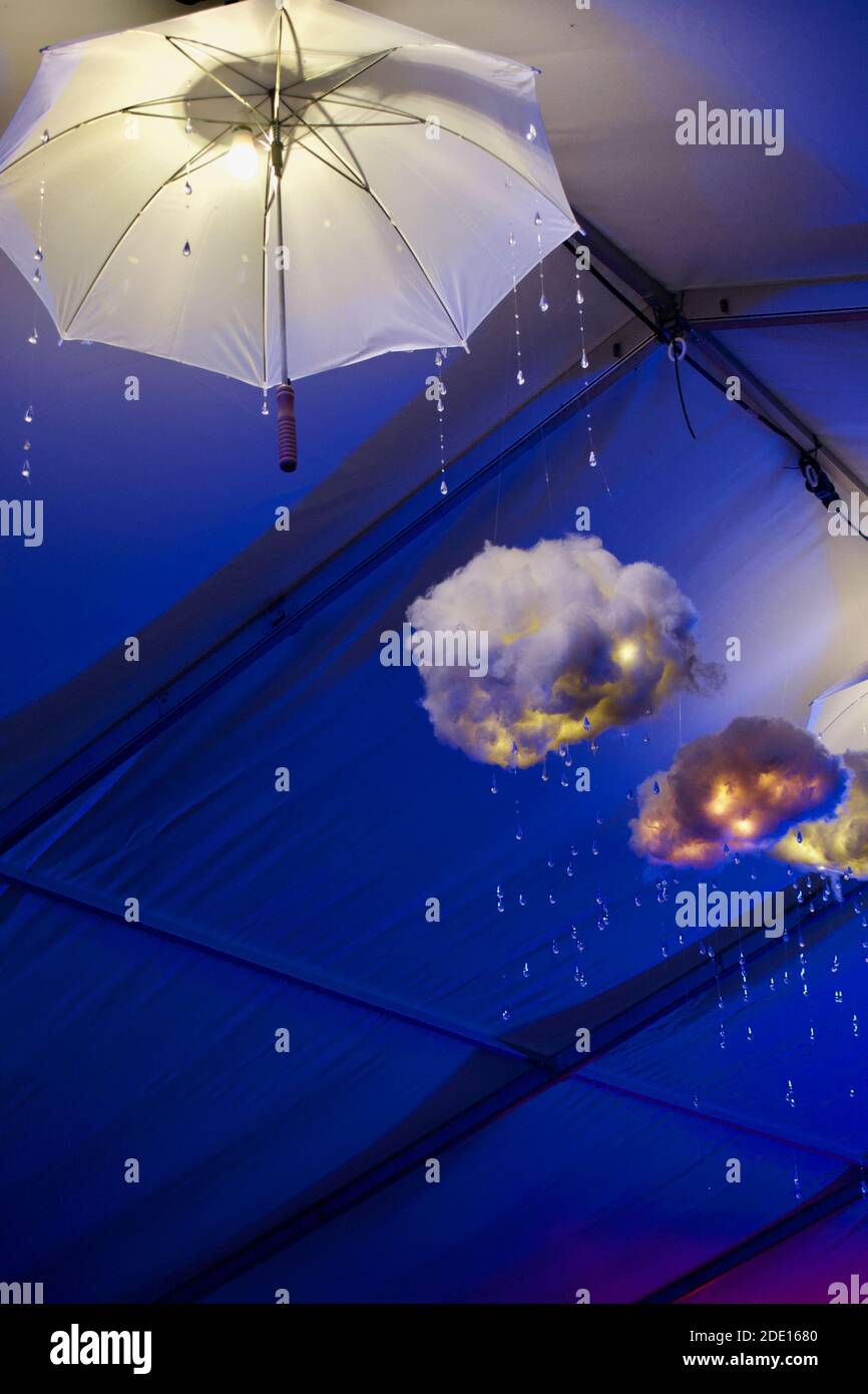 Umbrellas, fluffy clouds and raindrops lit blue and hanging from the ceiling: wet weather decorations Stock Photo