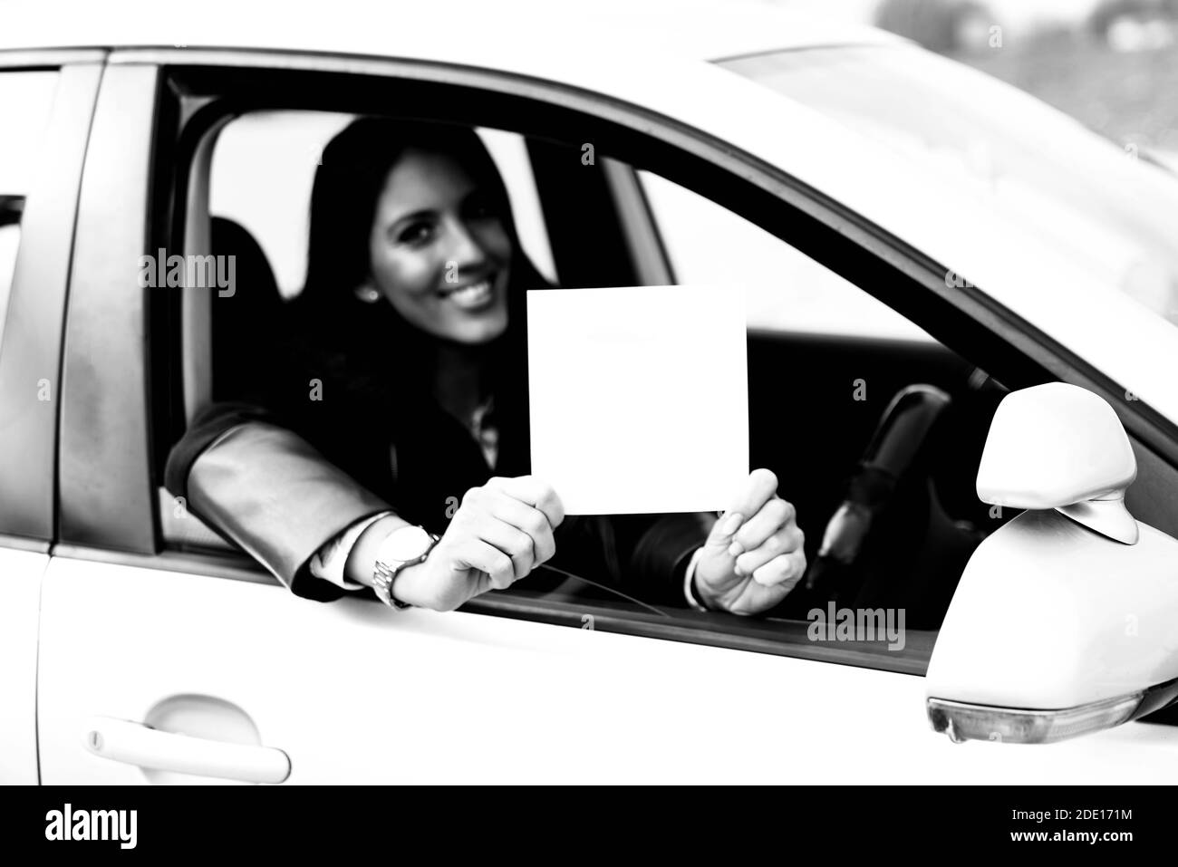Woman Sitting in the Car and Holding a White Blank Poster - Attractive Girl With a Clean Sheet of Paper or Your Text Stock Photo