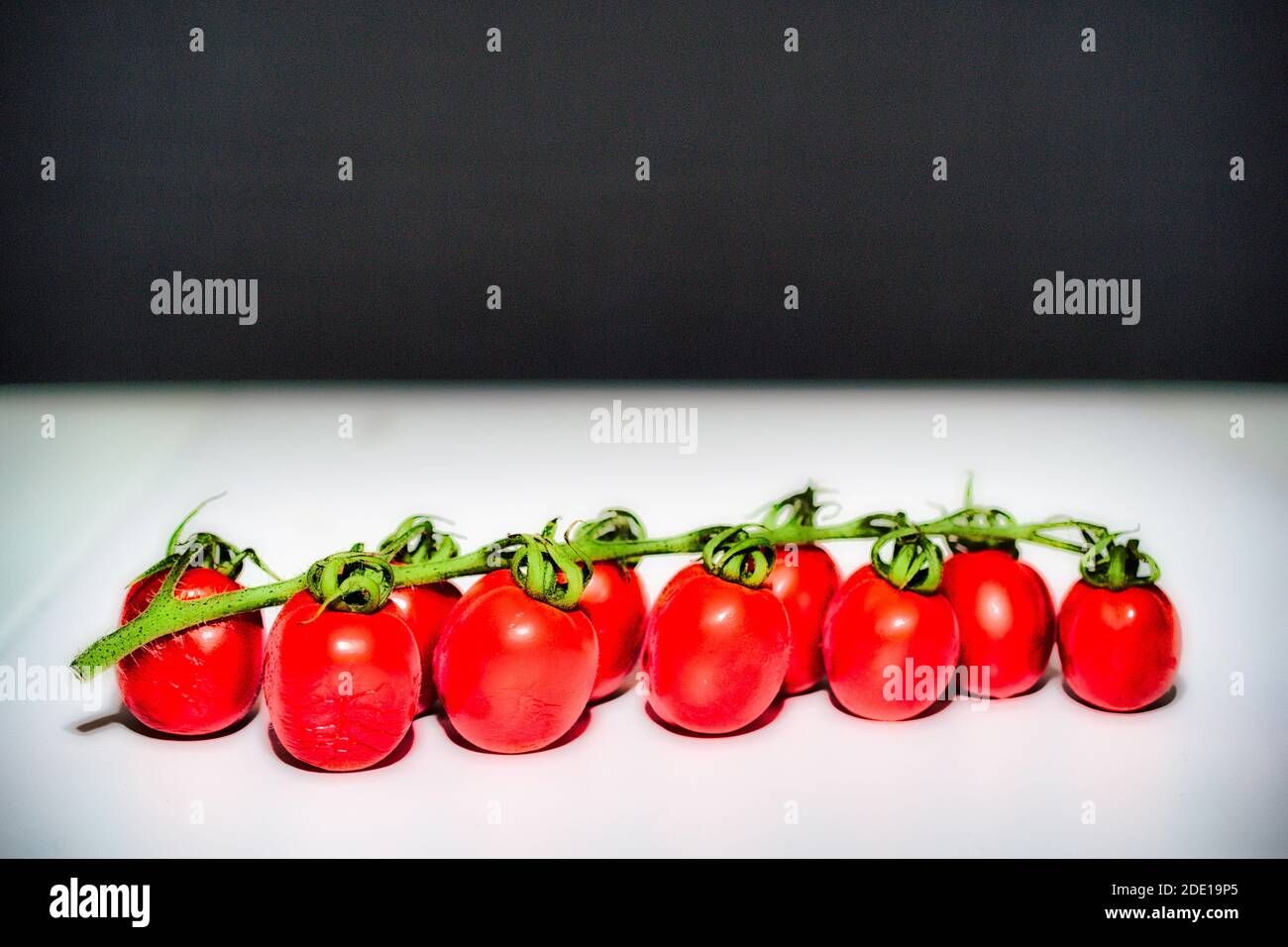 Cherry tomatoes on white table and black background Stock Photo