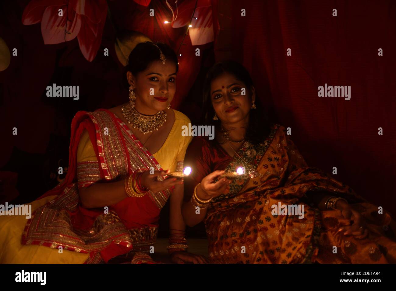 Two beautiful Indian Bengali women in Indian traditional dress lightening Diwali lamps sitting on the floor on Diwali evening. Indian lifestyle Stock Photo