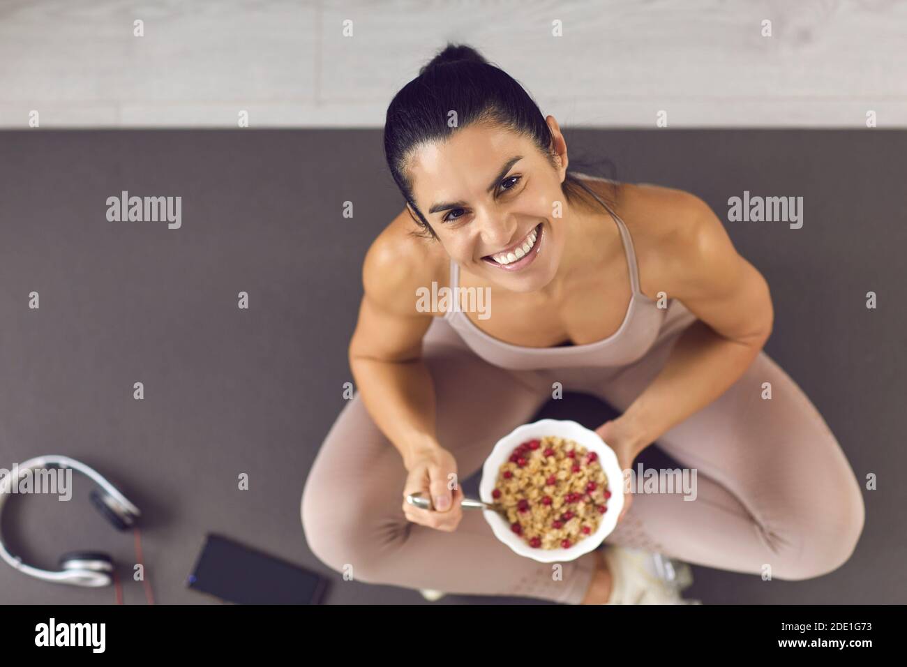 Happy fit woman sitting on a sports mat and enjoying healthy berry oatmeal muesli Stock Photo