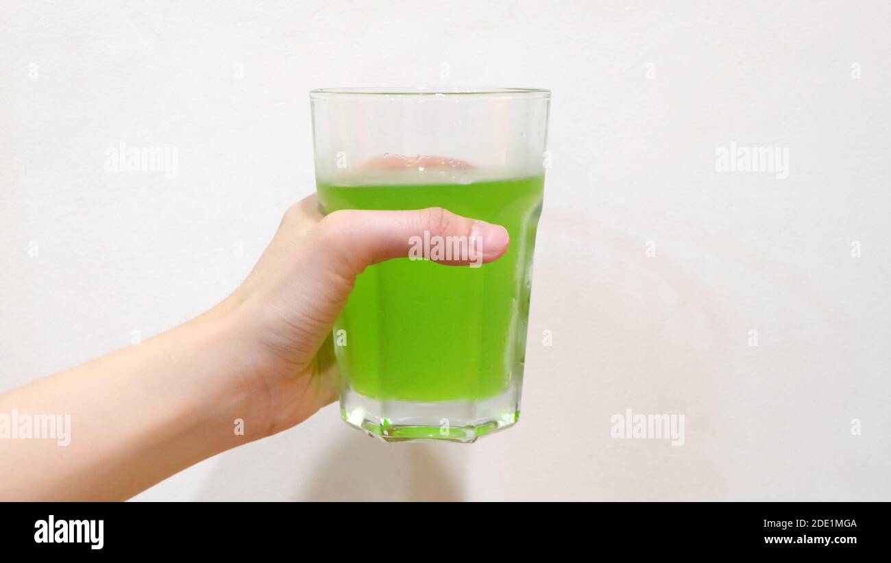 Hand holding a glass of vibrant green soda drink. Stock Photo