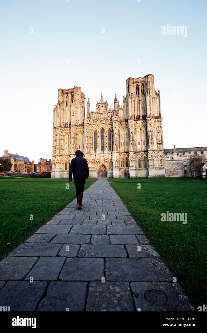 Mysterious figure walking on path towards cathedral building. Wells Cathedral. Somerset. UK. Stock Photo