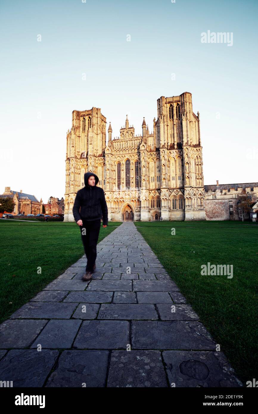 Mysterious figure walking on path away from cathedral building. Wells Cathedral. Somerset. UK. Stock Photo
