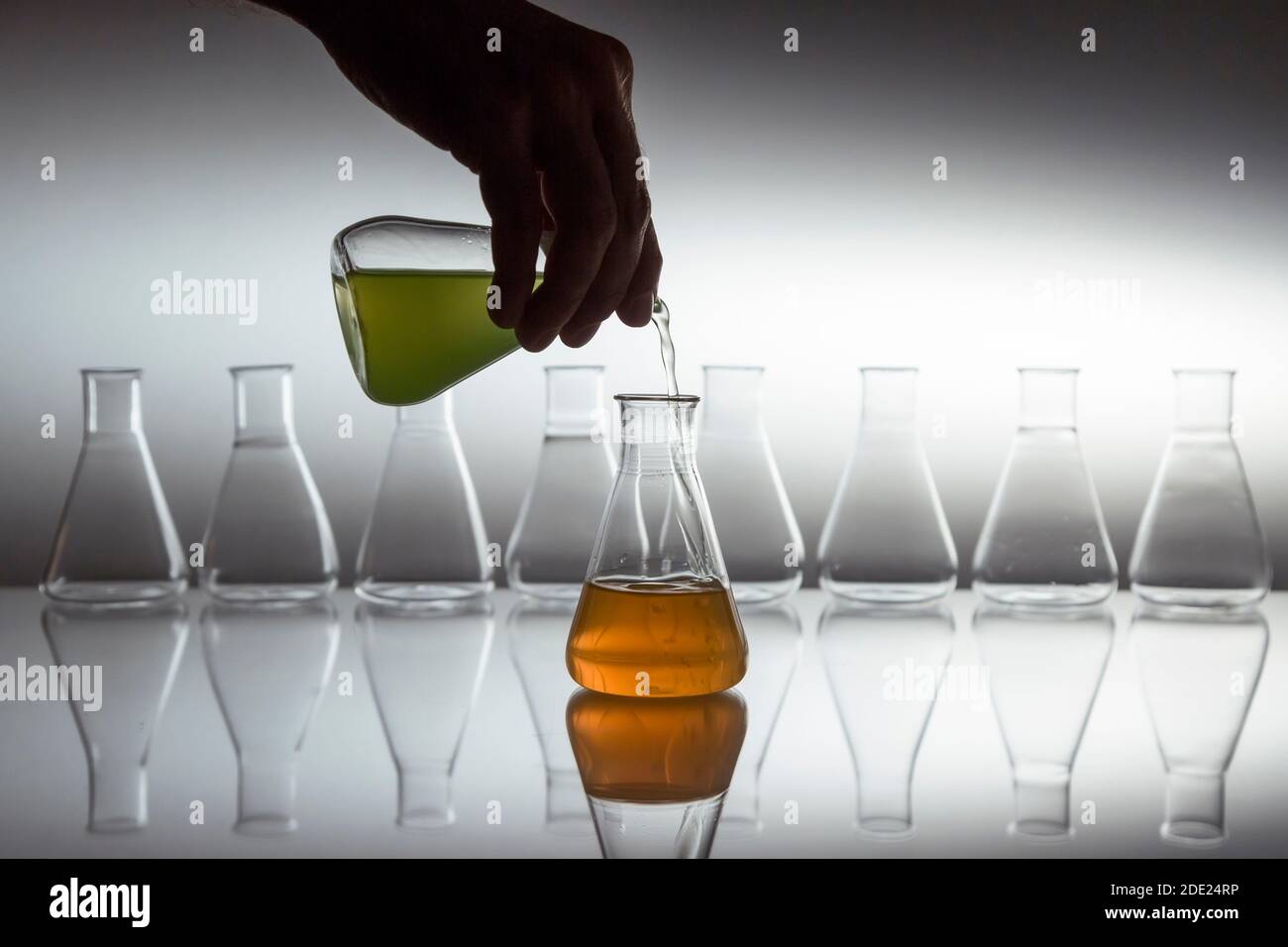Hand pouring green in to orange liquid in scientific laboratory glass ...