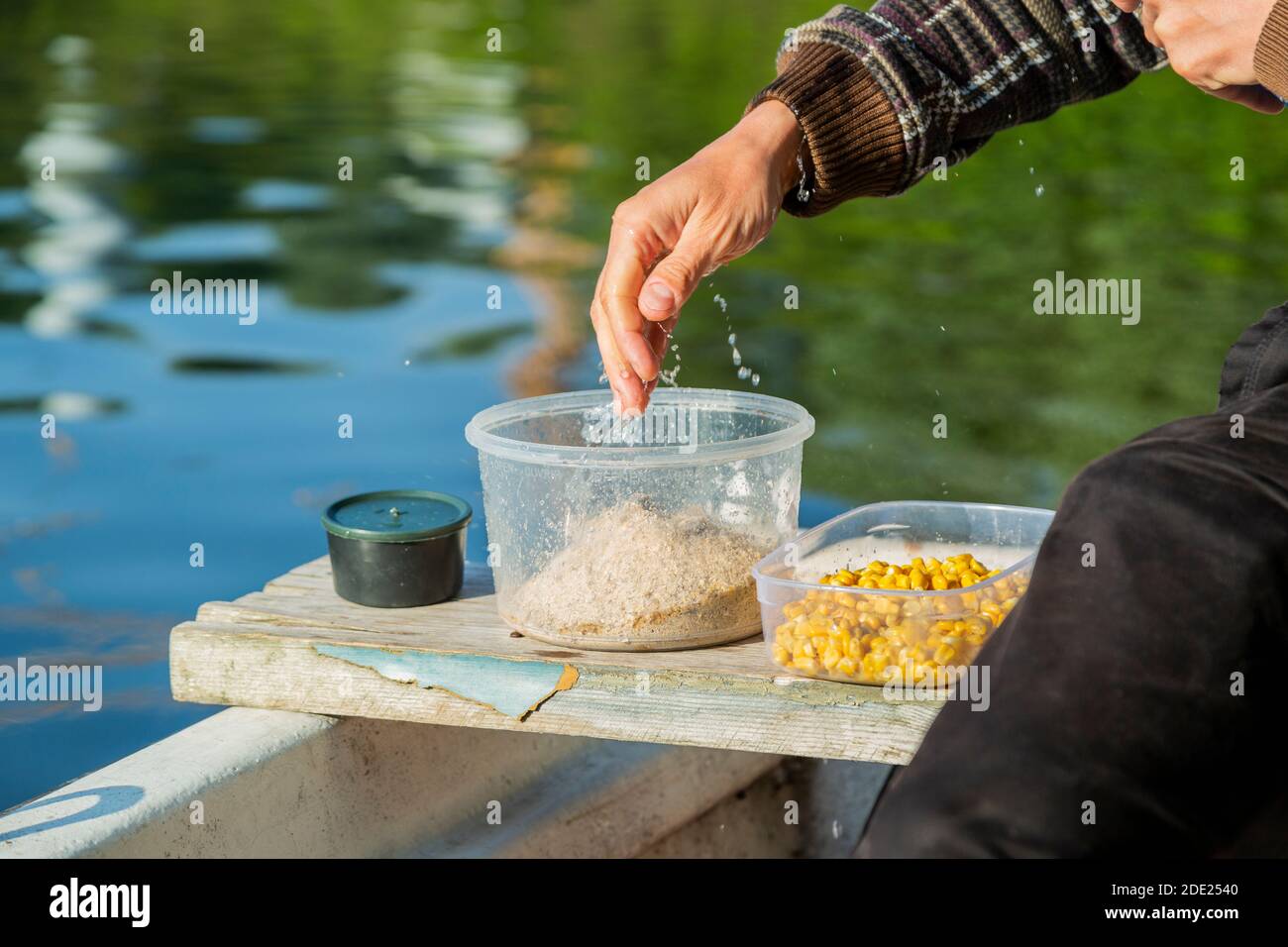 Hands making food for fish feeding and fishing chum. Man is adding corn and  mixing in plastic bowl. He is floating over river in white boat and sittin  Stock Photo - Alamy